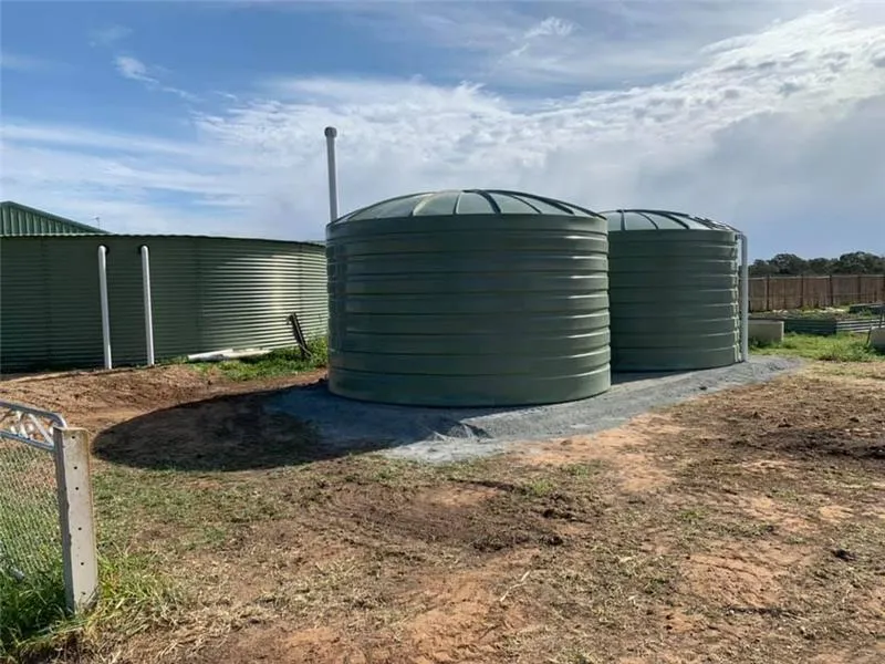 Two Bushmans round poly water tanks installed on a gravel base in a rural property setting