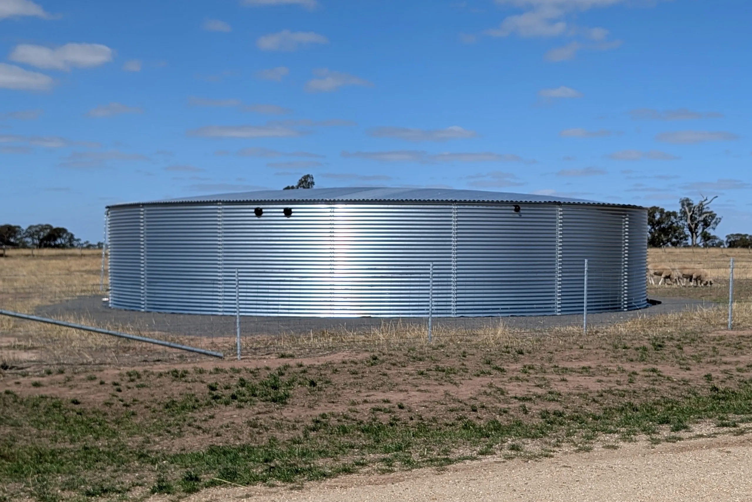 Large Waterline Aquamate Maxitank corrugated galvanised steel water tank enclosed by a fence on a rural Australian sheep property